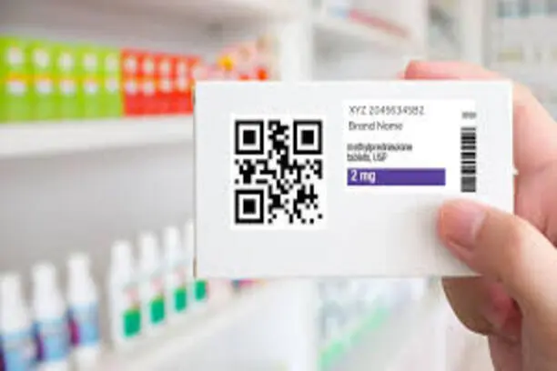 Close-up of a hand holding a medicine box with a QR code and prescription details in a pharmacy.